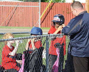 A coach helps a young Leduc Minor Softball player don a helmet to enhance player safety..